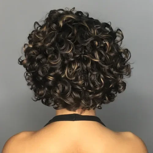 Short rounded curly bob with tight ringlets and caramel-toned highlights over dark brown.