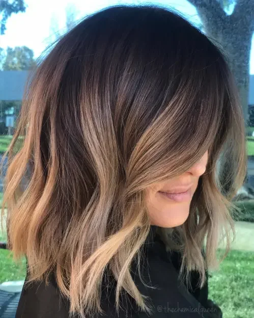 Shoulder-length lob with dark roots and caramel-beige balayage ribbons, side-swept for a glossy finish.