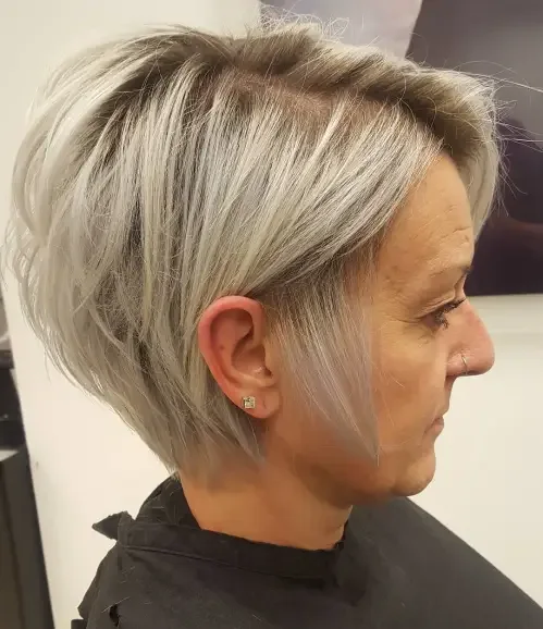 Elongated blonde pixie bob with longer crown and light forward fringe, softly layered sides, natural tousled finish.