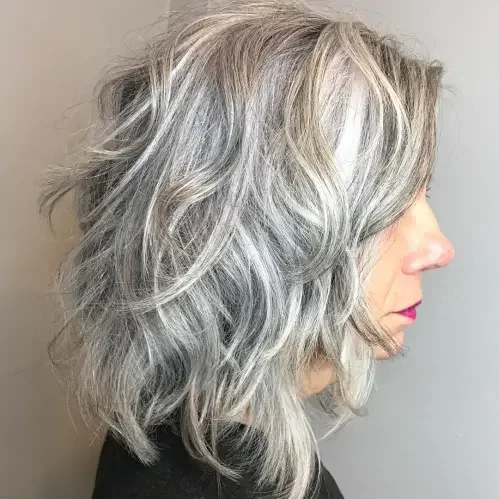 Silvery gray curly shag bob with layered shape and wispy side-swept fringe.