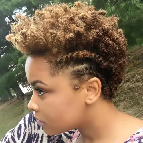 Curly faux hawk with side plaits and close-tapered sides, lifted crown, golden-brown natural texture.