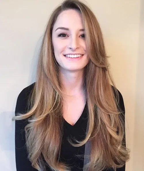 Long warm light-brown layers with soft side framing and flippy ends, styled in loose waves.