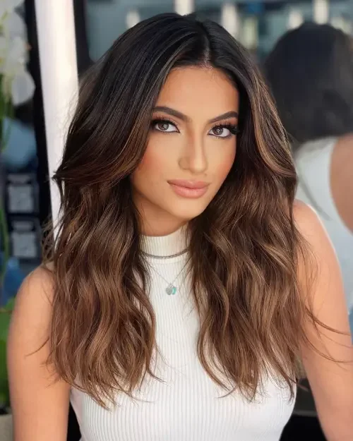 Long center-part waves with dark brown hair and warm caramel balayage highlights