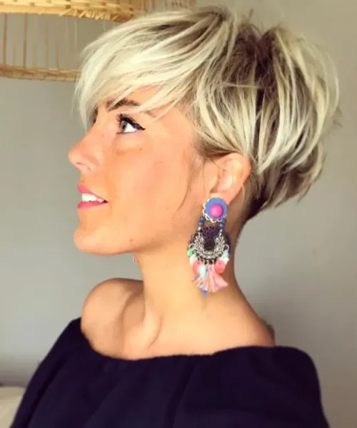 Voluminous ash-blonde pixie with darker roots, wispy side-swept fringe, and close cropped undercut back.