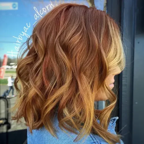 Copper strawberry blonde shoulder-length waves with face-framing blonde money pieces and layered shape.