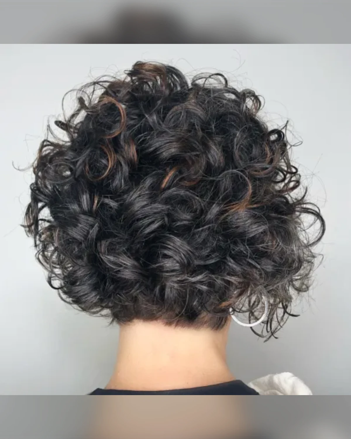 Rounded chin-length curly bob with perm-style ringlets in dark brown with subtle highlights.